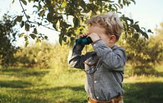 enfant tenant des jumelles à côté d'un arbre